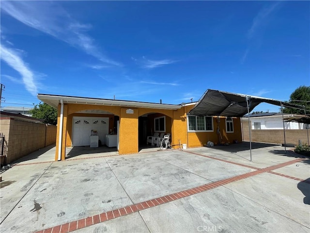 view of front facade with stucco siding, an attached garage, a detached carport, and fence