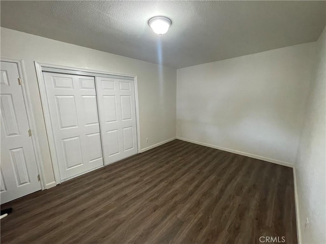 unfurnished bedroom featuring a textured ceiling, baseboards, a closet, and dark wood-style floors