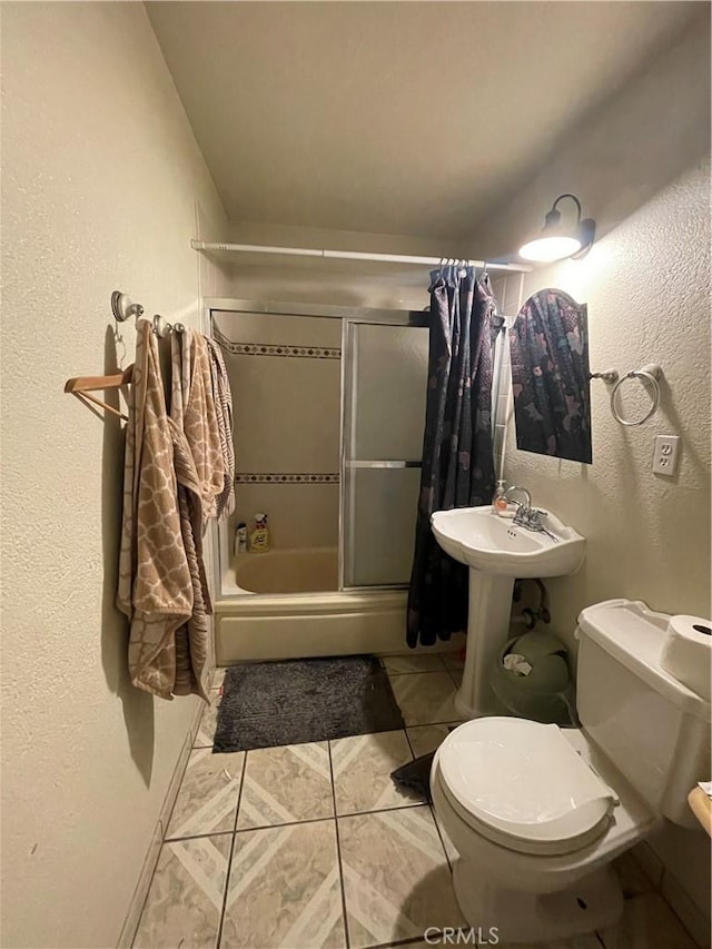 full bath with tile patterned floors, a sink, a textured wall, enclosed tub / shower combo, and toilet