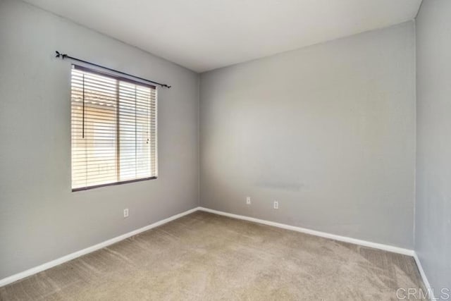 spare room with baseboards and light colored carpet