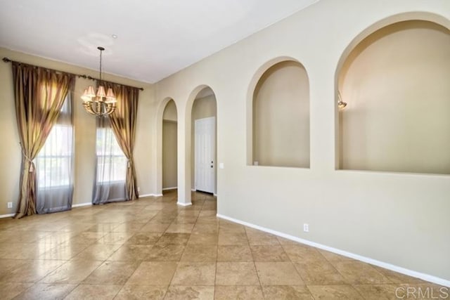 unfurnished room with a chandelier, arched walkways, and baseboards