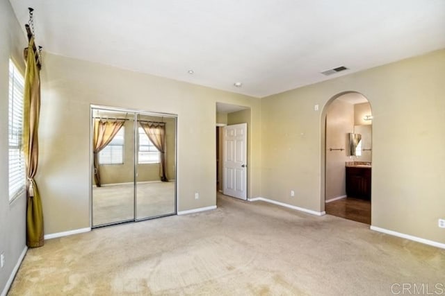 unfurnished bedroom featuring arched walkways, baseboards, visible vents, and light colored carpet