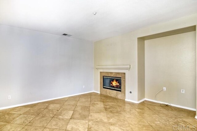 unfurnished living room featuring a tiled fireplace, baseboards, and visible vents