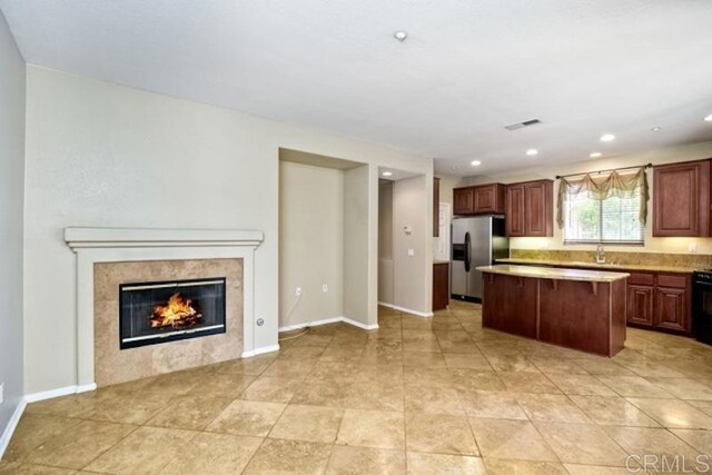 kitchen with a tiled fireplace, stove, light countertops, a center island, and stainless steel refrigerator with ice dispenser