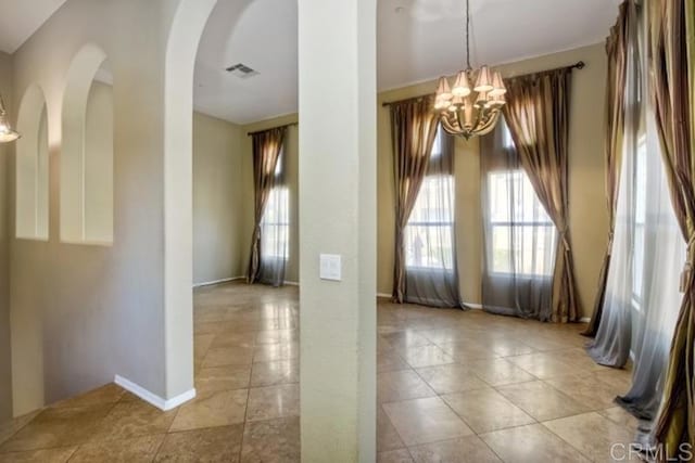 spare room featuring visible vents, arched walkways, a notable chandelier, and light tile patterned floors