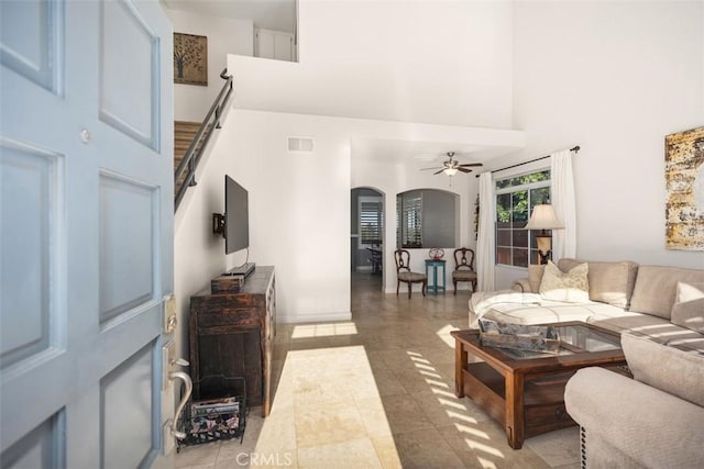 living area with stairway, a towering ceiling, visible vents, arched walkways, and ceiling fan