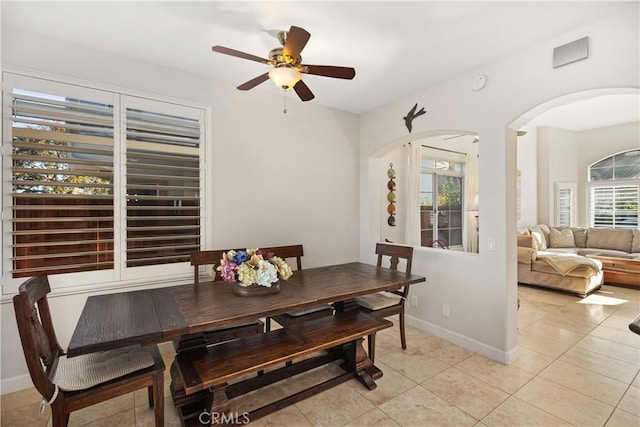 dining area with arched walkways, a ceiling fan, baseboards, and light tile patterned floors