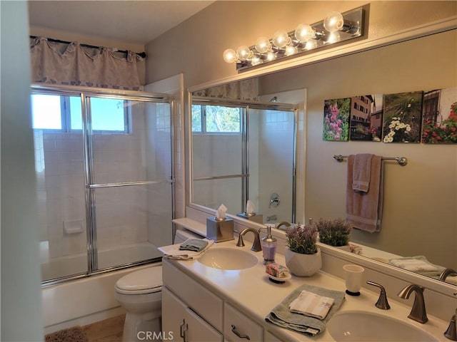 full bath featuring shower / bath combination with glass door, toilet, double vanity, and a sink