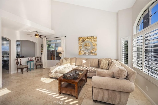 living room with light tile patterned floors, ceiling fan, arched walkways, baseboards, and a high ceiling