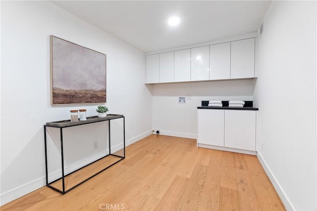 clothes washing area featuring light wood-type flooring, baseboards, visible vents, washer hookup, and cabinet space