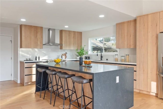 kitchen with modern cabinets, wall chimney range hood, light brown cabinetry, and a sink