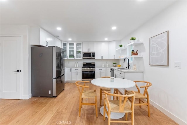 kitchen featuring open shelves, a sink, light wood-style floors, stainless steel appliances, and white cabinetry