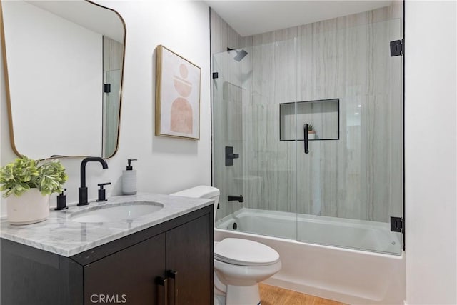 bathroom with wood finished floors, vanity, toilet, and bath / shower combo with glass door