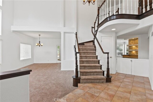 staircase with a towering ceiling, a notable chandelier, and carpet flooring