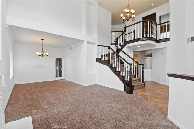 carpeted entrance foyer featuring baseboards, a high ceiling, an inviting chandelier, and stairs