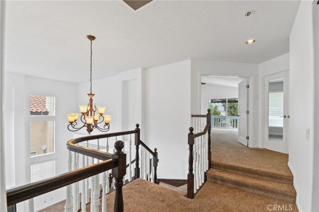 corridor featuring carpet flooring, baseboards, visible vents, a notable chandelier, and an upstairs landing