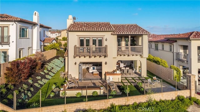 rear view of property featuring stucco siding, a fenced backyard, a patio area, a balcony, and a tiled roof
