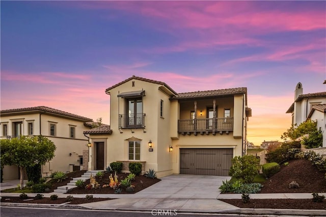 mediterranean / spanish-style house with an attached garage, stucco siding, concrete driveway, a balcony, and a tiled roof