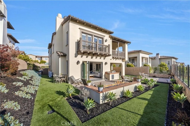 back of house featuring fence, a balcony, a yard, a patio, and stucco siding
