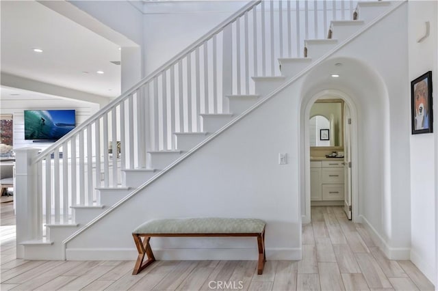 stairs with baseboards, arched walkways, wood finished floors, and recessed lighting