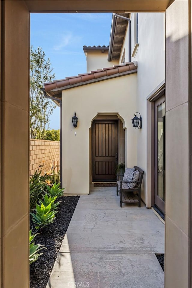 entrance to property featuring stucco siding and fence