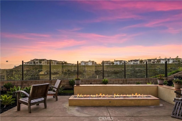 patio terrace at dusk featuring a residential view, a fenced backyard, and an outdoor fire pit