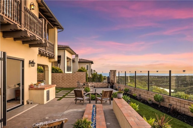 patio terrace at dusk featuring a water view, fence, and an outdoor hangout area