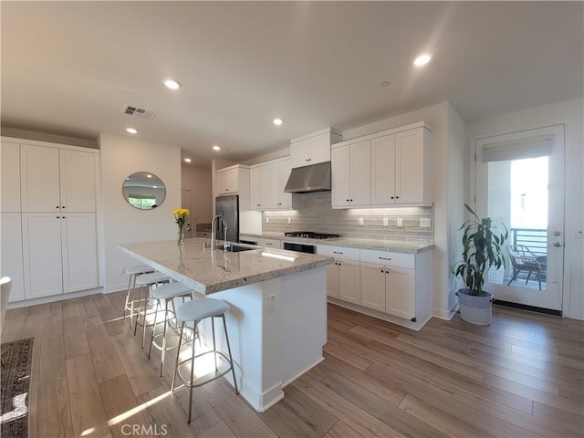 27078 Painted Sky Way, Valencia, CA 91381 - kitchen with under cabinet range hood, tasteful backsplash, gas stovetop, light wood finished floors, and a kitchen island with sink