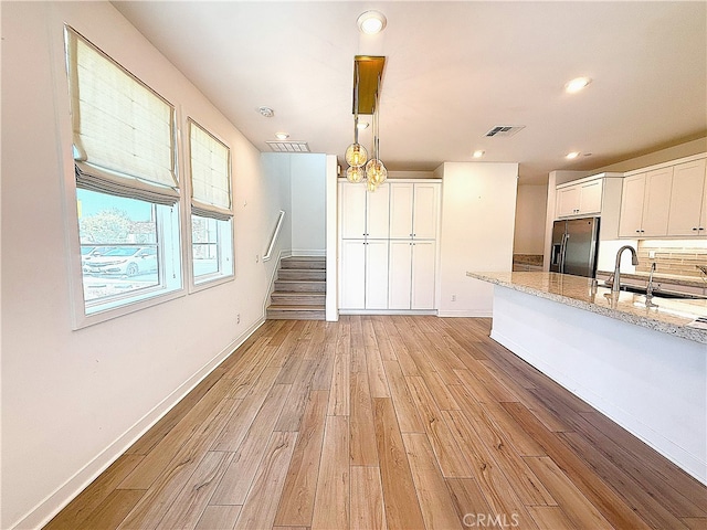 27078 Painted Sky Way, Valencia, CA 91381 - kitchen featuring stainless steel refrigerator with ice dispenser, a sink, light wood-style flooring, white cabinetry, and light stone countertops