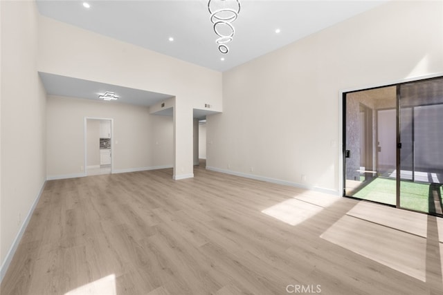 unfurnished living room featuring baseboards, recessed lighting, a high ceiling, and light wood-style flooring