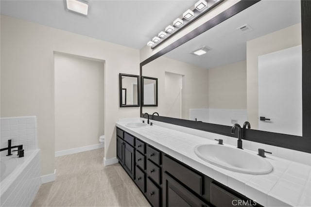 bathroom featuring double vanity, toilet, a bath, a sink, and baseboards