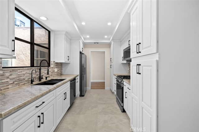 kitchen with light stone counters, black appliances, backsplash, a sink, and white cabinetry