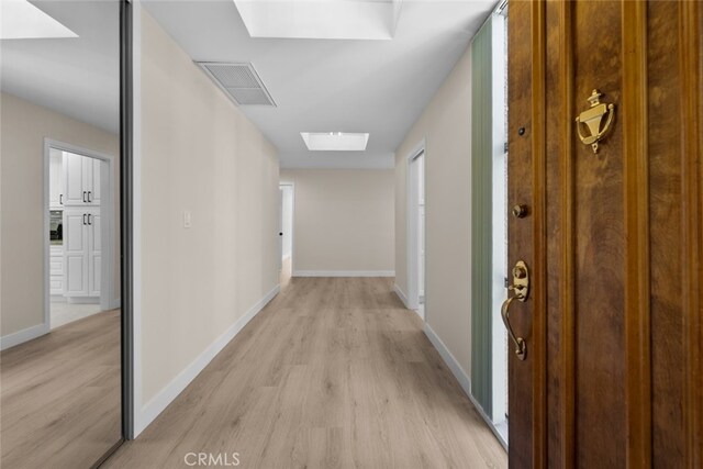corridor with a skylight, visible vents, baseboards, and light wood-type flooring