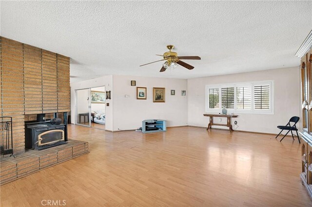 living area featuring a wood stove, light wood-style floors, a textured ceiling, and ceiling fan