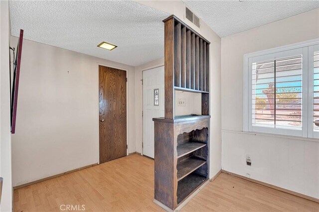 interior space featuring wood finished floors, a textured ceiling, baseboards, and visible vents
