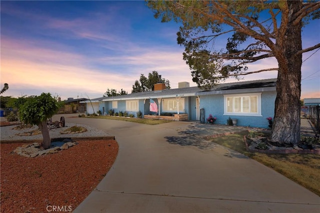 view of front facade featuring a chimney, stucco siding, and curved driveway