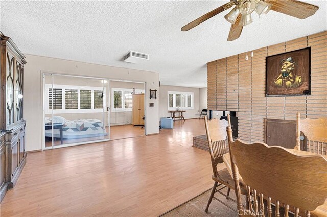dining space with a textured ceiling, visible vents, a ceiling fan, light wood-style flooring, and a brick fireplace