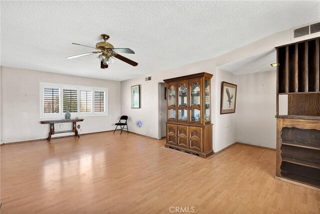 interior space featuring light wood finished floors, a ceiling fan, visible vents, and a textured ceiling