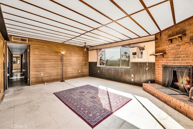 unfurnished living room with wainscoting, visible vents, a brick fireplace, and wooden walls