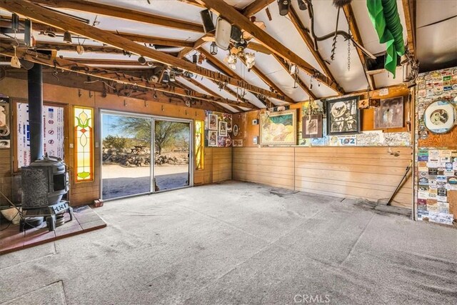 unfurnished living room with wooden walls, vaulted ceiling, a wood stove, and carpet flooring