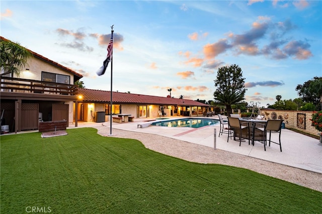 pool at dusk featuring a patio, a fenced in pool, and a lawn