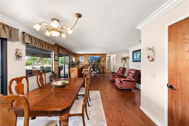 dining area with wood finished floors, a notable chandelier, crown molding, and a brick fireplace