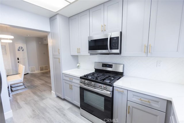2196 Evergreen Dr, Tustin, CA 92782 - kitchen with appliances with stainless steel finishes, gray cabinets, light wood-style floors, backsplash, and light stone counters