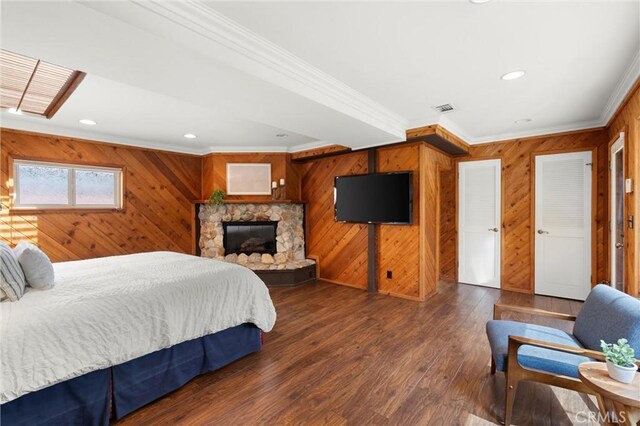 bedroom with visible vents, recessed lighting, wood walls, crown molding, and a stone fireplace