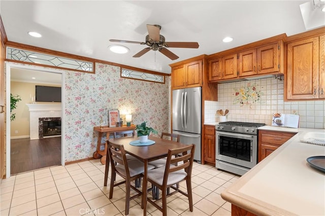 kitchen featuring stainless steel appliances, light countertops, ornamental molding, brown cabinetry, and ceiling fan