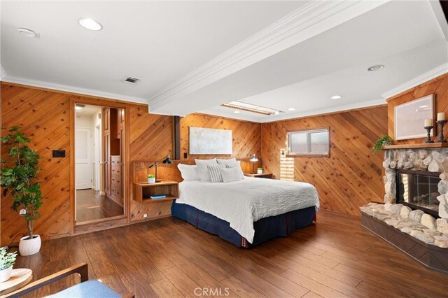 bedroom with crown molding, hardwood / wood-style flooring, a fireplace, wood walls, and visible vents