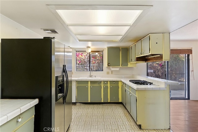 kitchen featuring stainless steel refrigerator with ice dispenser, white gas stovetop, tile countertops, and a sink