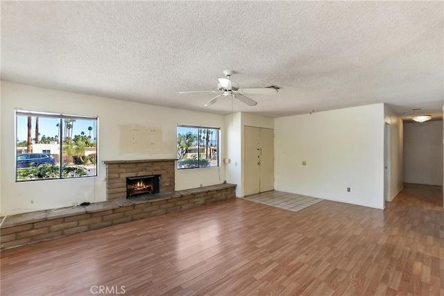 unfurnished living room with ceiling fan, a fireplace, light wood finished floors, and a textured ceiling