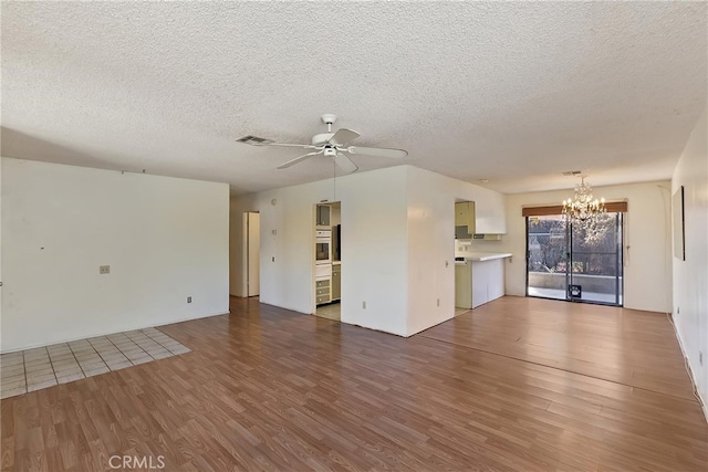 unfurnished living room with a textured ceiling, visible vents, wood finished floors, and ceiling fan with notable chandelier