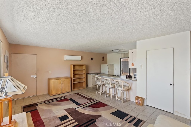 kitchen with a kitchen breakfast bar, a textured ceiling, freestanding refrigerator, a wall unit AC, and light tile patterned floors